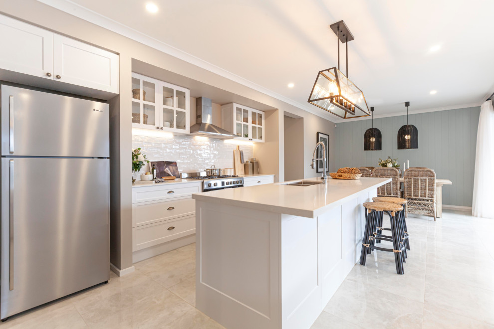 Large beach style galley open plan kitchen in Melbourne with a double-bowl sink, white cabinets, quartz benchtops, white splashback, ceramic splashback, stainless steel appliances, ceramic floors, with island, beige floor and white benchtop.