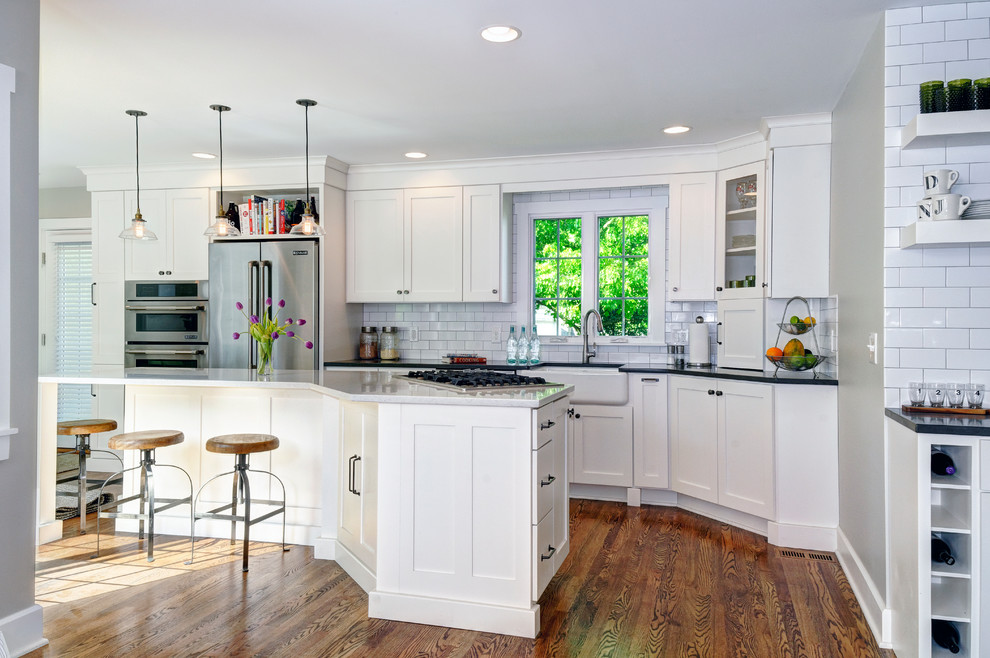 Design ideas for a traditional eat-in kitchen in Columbus with a farmhouse sink, white cabinets, quartz benchtops, white splashback, subway tile splashback, stainless steel appliances, dark hardwood floors, with island and shaker cabinets.