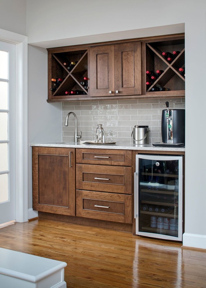 Photo of a small transitional single-wall wet bar in DC Metro with an undermount sink, medium wood cabinets, quartzite benchtops, grey splashback, glass tile splashback, medium hardwood floors and recessed-panel cabinets.