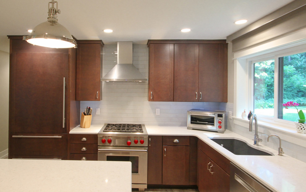 This is an example of a small modern l-shaped eat-in kitchen in Grand Rapids with an undermount sink, flat-panel cabinets, brown cabinets, quartz benchtops, white splashback, subway tile splashback, stainless steel appliances, light hardwood floors and with island.