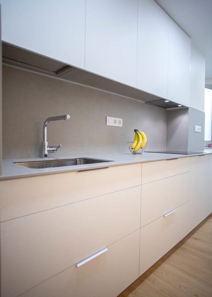 This is an example of a large modern galley separate kitchen in Barcelona with a single-bowl sink, flat-panel cabinets, beige cabinets, grey splashback, stainless steel appliances, medium hardwood floors, no island, brown floor and grey benchtop.