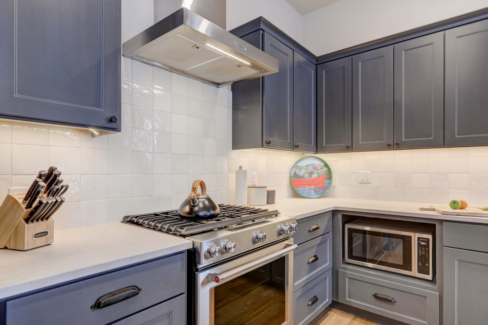 Foto på ett mellanstort vintage beige kök med öppen planlösning, med skåp i shakerstil, blå skåp, bänkskiva i kvarts, vitt stänkskydd, stänkskydd i porslinskakel, rostfria vitvaror, mellanmörkt trägolv, en köksö och brunt golv