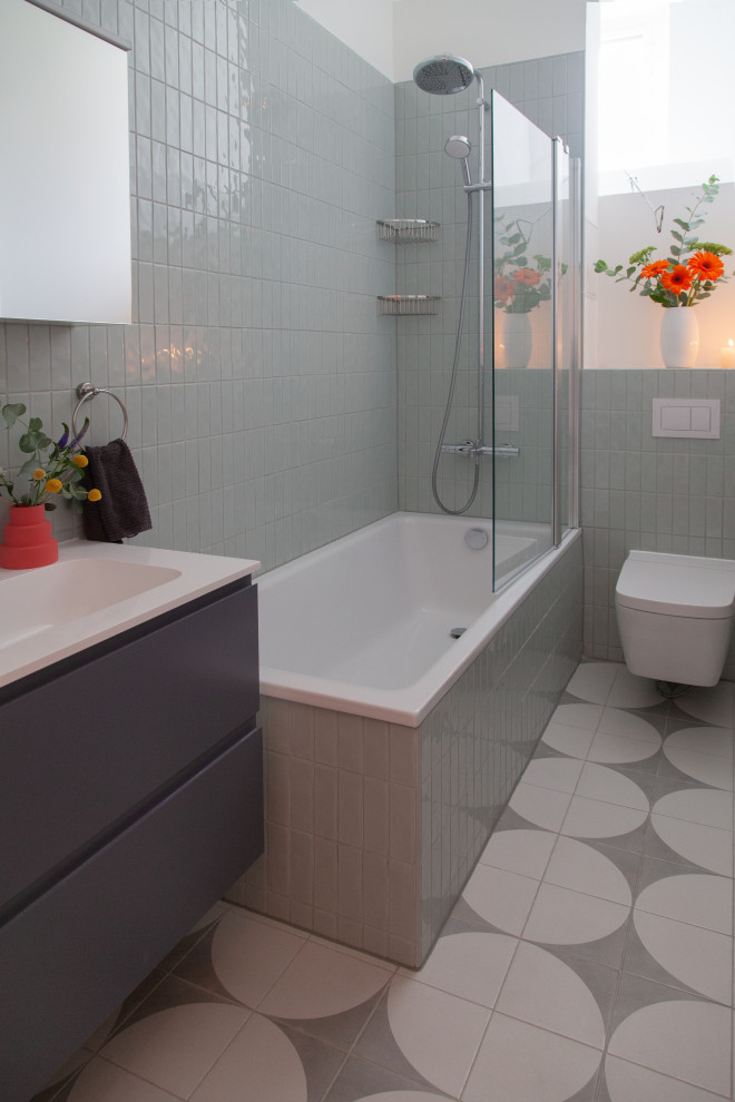 На фото: узкая и длинная серо-белая ванная комната среднего размера в современном стиле с фасадами с выступающей филенкой, серыми фасадами, накладной ванной, душем над ванной, раздельным унитазом, зеленой плиткой, керамической плиткой, белыми стенами, полом из керамической плитки, душевой кабиной, монолитной раковиной, столешницей из ламината, серым полом, открытым душем, белой столешницей, тумбой под одну раковину, подвесной тумбой и многоуровневым потолком