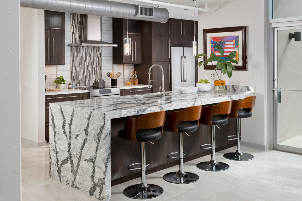 This is an example of an industrial kitchen in Houston with an undermount sink, flat-panel cabinets, dark wood cabinets, granite benchtops, stainless steel appliances, marble floors, multi-coloured splashback, mosaic tile splashback and a peninsula.