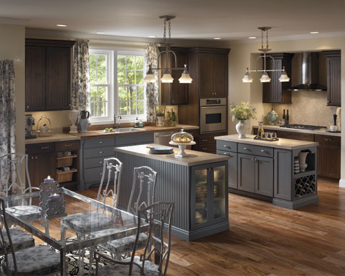 Design ideas for a large traditional l-shaped eat-in kitchen in Other with louvered cabinets, brown cabinets, a drop-in sink, granite benchtops, beige splashback, ceramic splashback, stainless steel appliances, light hardwood floors and multiple islands.