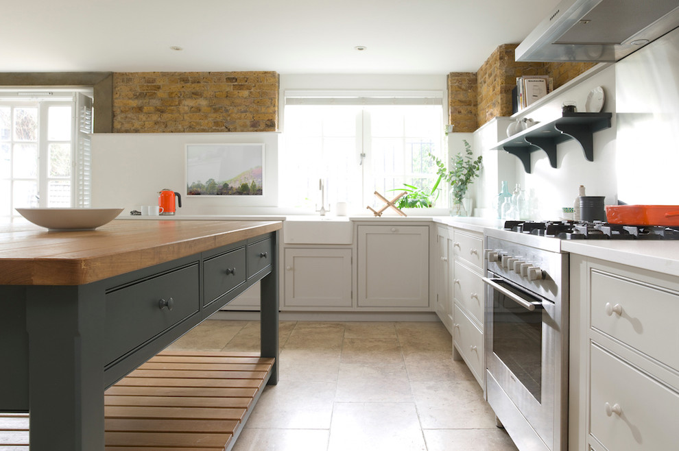 Design ideas for a mid-sized transitional l-shaped open plan kitchen in London with a farmhouse sink, flat-panel cabinets, grey cabinets, granite benchtops, metallic splashback, stainless steel appliances, travertine floors and with island.