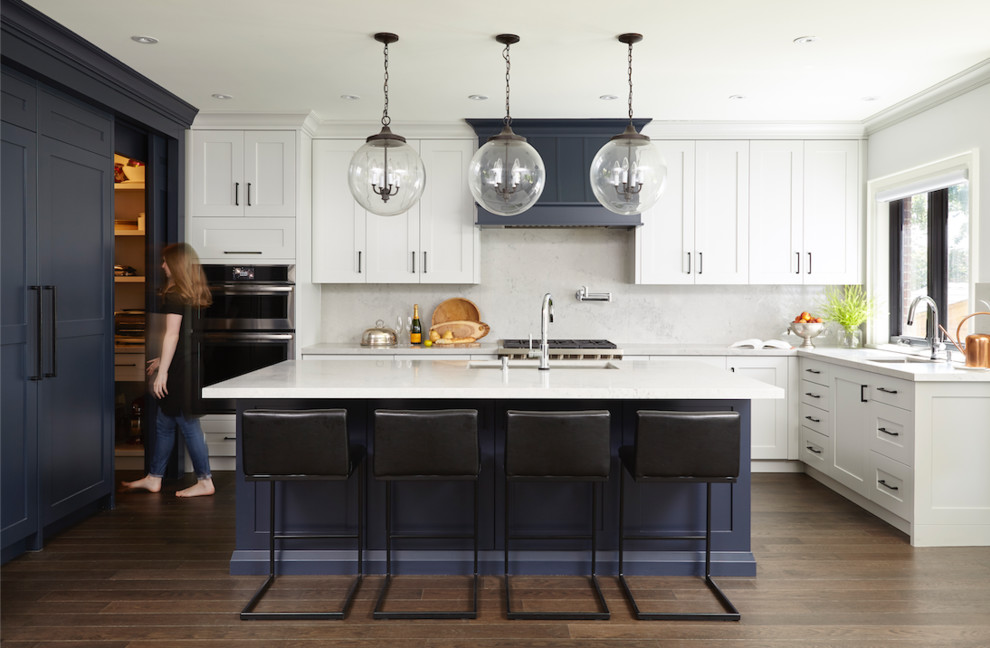 Large transitional u-shaped dark wood floor and brown floor kitchen photo in Toronto with an undermount sink, shaker cabinets, white cabinets, white backsplash, stainless steel appliances, an island and white countertops