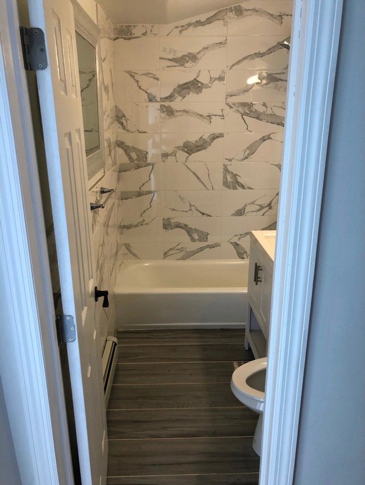 This is an example of a small contemporary bathroom in New York with shaker cabinets, grey cabinets, an alcove tub, a shower/bathtub combo, a two-piece toilet, white tile, marble, white walls, porcelain floors, an integrated sink, solid surface benchtops, grey floor, an open shower and white benchtops.