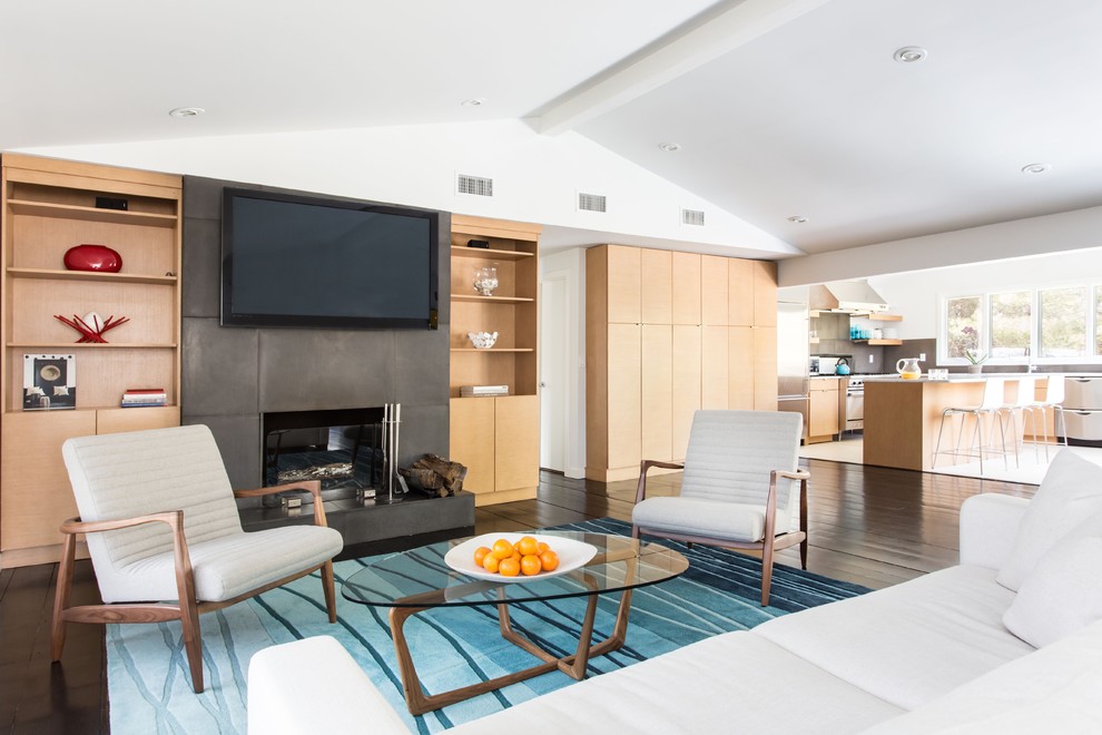 This is an example of a contemporary open concept living room in New York with white walls, dark hardwood floors, a standard fireplace and a wall-mounted tv.