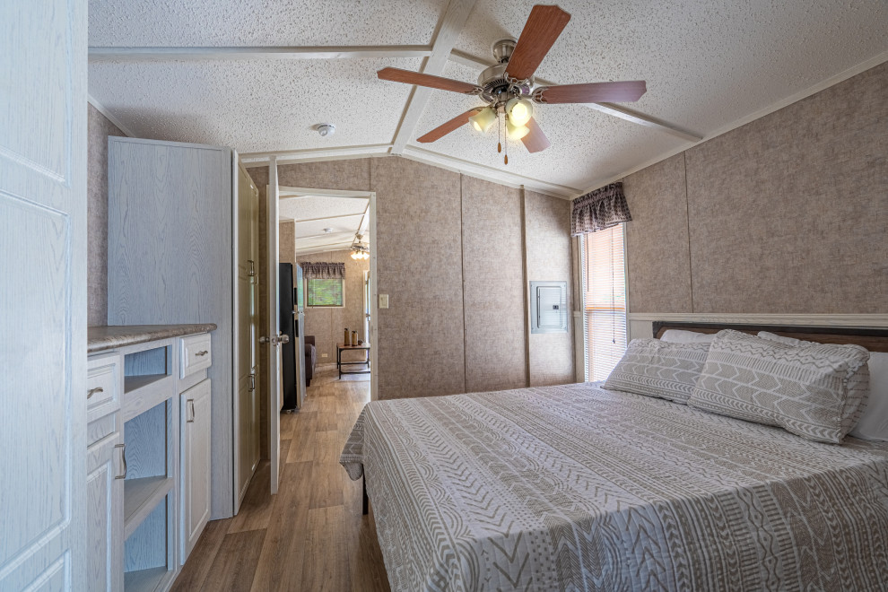 Imagen de dormitorio principal de estilo de casa de campo pequeño sin chimenea con paredes beige, suelo de linóleo, suelo marrón, vigas vistas y panelado