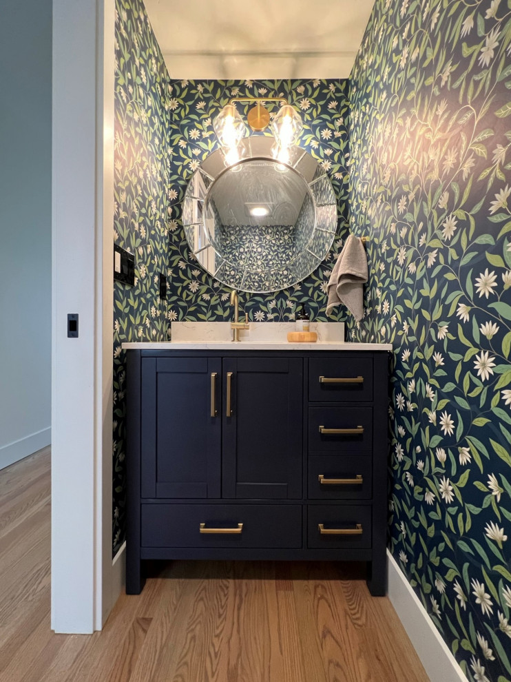 Cette image montre un petit WC et toilettes traditionnel avec un placard à porte shaker, des portes de placard bleues, un mur bleu, un sol en bois brun, un lavabo encastré, un sol marron, un plan de toilette blanc, meuble-lavabo encastré et du papier peint.