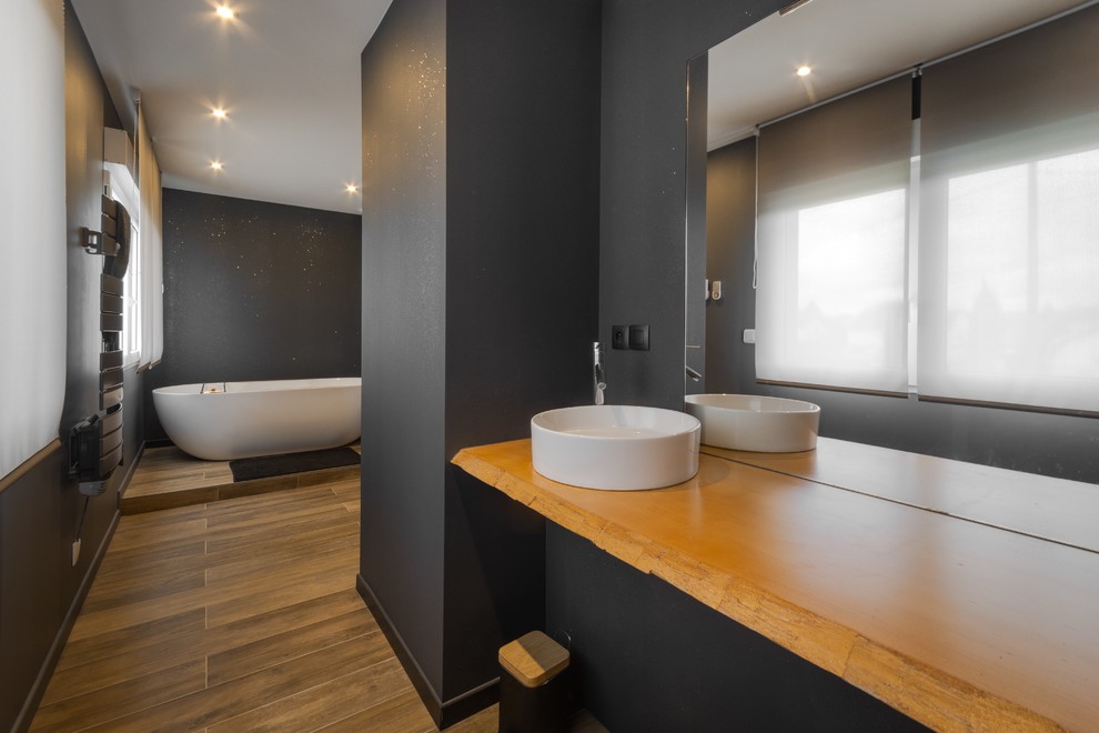 Inspiration for a contemporary bathroom in Other with a freestanding tub, black walls, a vessel sink, wood benchtops, brown floor and brown benchtops.