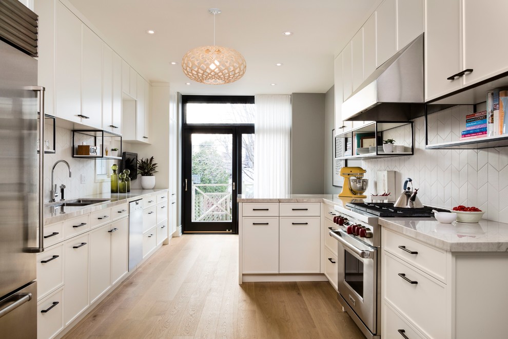 This is an example of a mid-sized transitional galley separate kitchen in Toronto with an undermount sink, recessed-panel cabinets, white cabinets, quartzite benchtops, white splashback, ceramic splashback, stainless steel appliances, light hardwood floors and a peninsula.