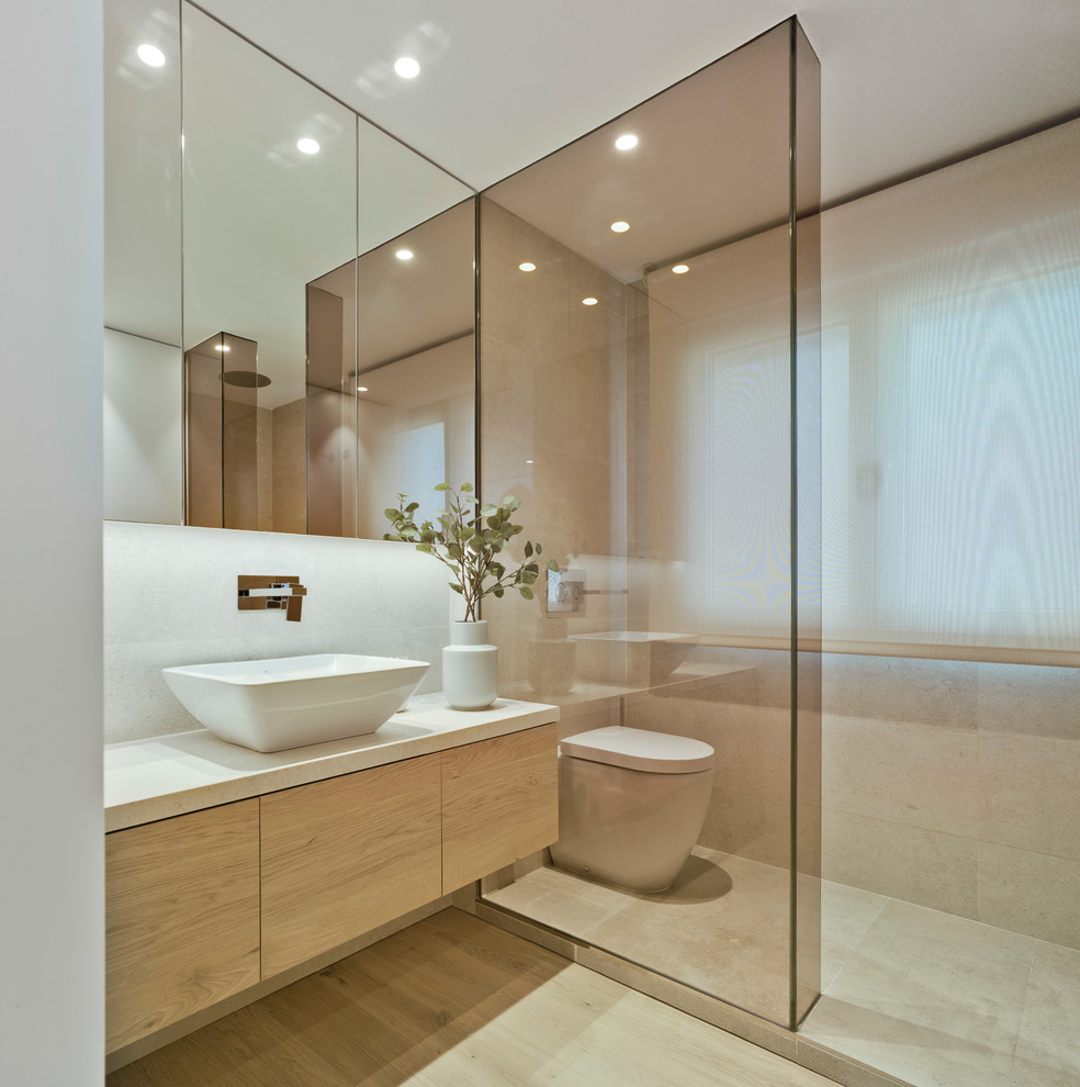 Photo of a contemporary powder room in Other with flat-panel cabinets, a vessel sink, white benchtops, light wood cabinets, a wall-mount toilet, white walls and beige floor.