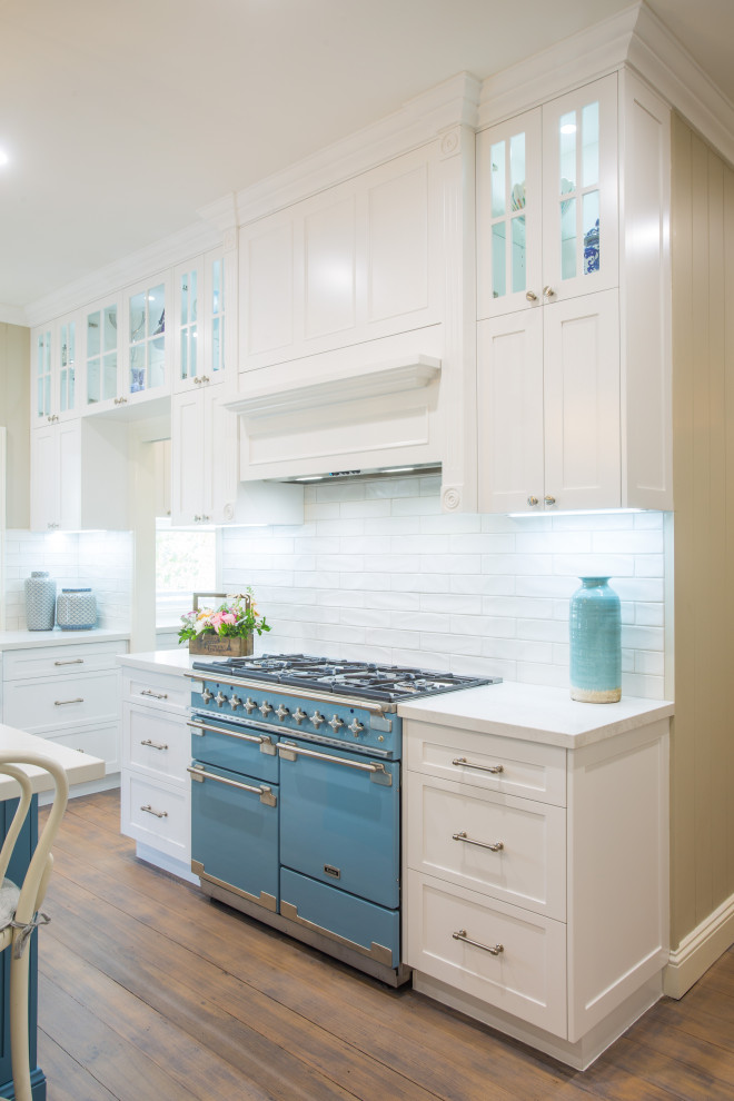 Design ideas for an expansive traditional l-shaped kitchen pantry in Brisbane with a farmhouse sink, shaker cabinets, white cabinets, quartz benchtops, white splashback, subway tile splashback, coloured appliances, medium hardwood floors, with island and white benchtop.