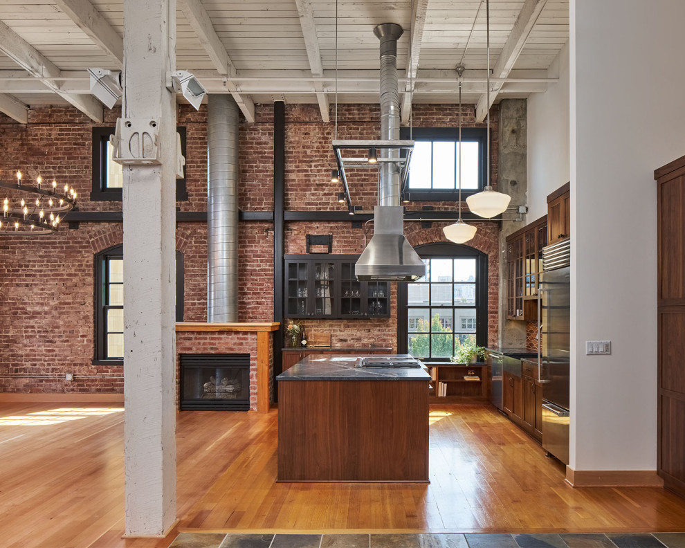 Photo of a mid-sized industrial l-shaped open plan kitchen in Portland with a farmhouse sink, glass-front cabinets, dark wood cabinets, soapstone benchtops, multi-coloured splashback, ceramic splashback, stainless steel appliances, medium hardwood floors, with island, brown floor, black benchtop and exposed beam.