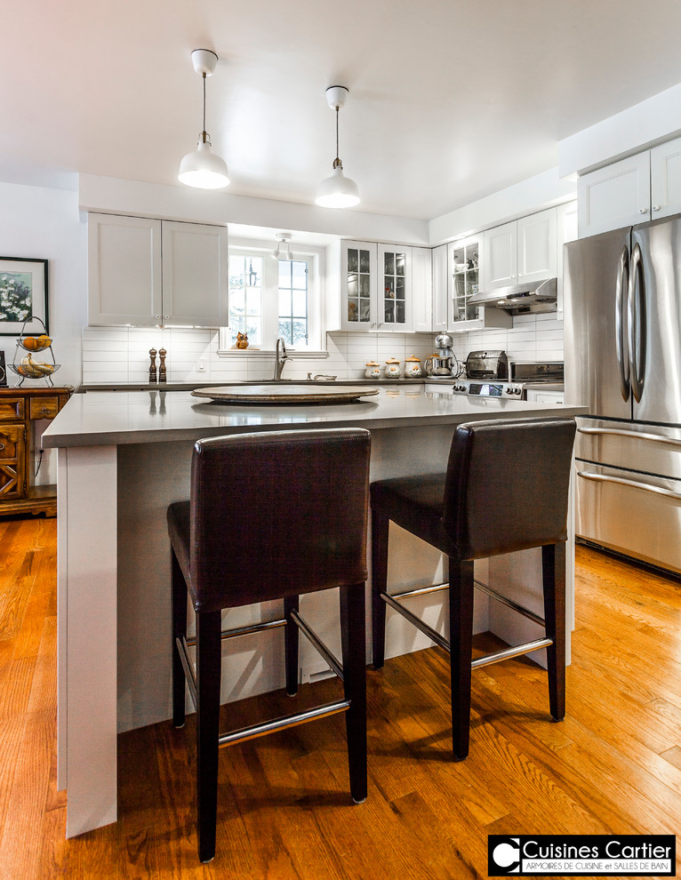 Eat-in kitchen - large transitional medium tone wood floor eat-in kitchen idea in Montreal with a double-bowl sink, shaker cabinets, white cabinets, quartzite countertops, white backsplash, ceramic backsplash, stainless steel appliances and an island