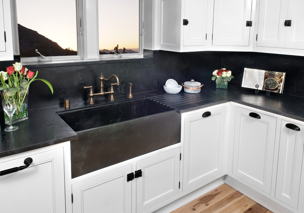 Inspiration for a traditional kitchen in San Diego with a farmhouse sink, beaded inset cabinets, white cabinets, soapstone benchtops, black splashback, stone slab splashback, bamboo floors, orange floor and black benchtop.