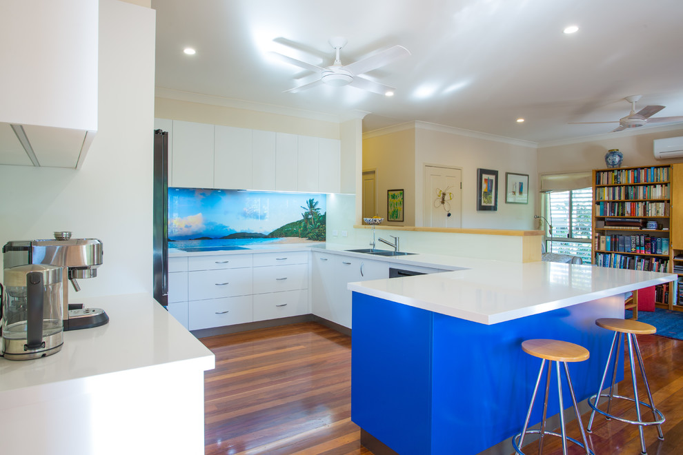 Design ideas for a mid-sized beach style u-shaped kitchen pantry in Brisbane with a double-bowl sink, flat-panel cabinets, blue cabinets, quartz benchtops, blue splashback, glass sheet splashback, stainless steel appliances, dark hardwood floors, with island, brown floor and white benchtop.