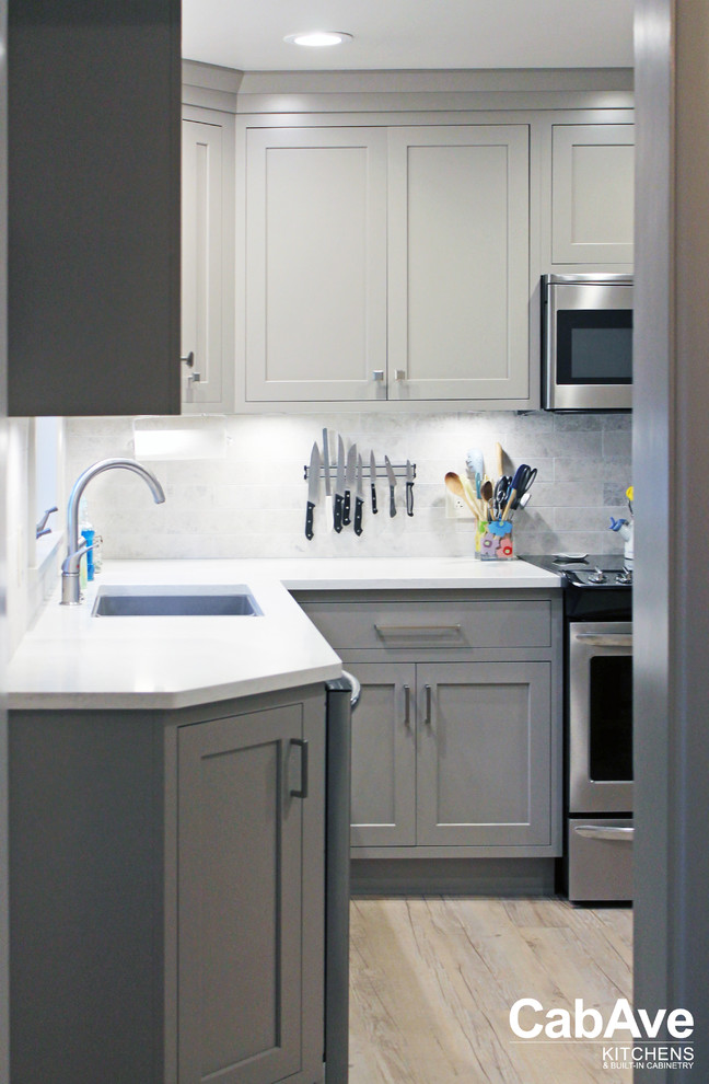 Inspiration for a small transitional l-shaped vinyl floor and brown floor enclosed kitchen remodel with an undermount sink, recessed-panel cabinets, gray cabinets, quartz countertops, white backsplash, subway tile backsplash, stainless steel appliances and no island