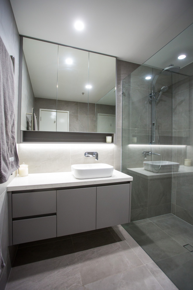 Inspiration for a mid-sized modern kids bathroom in Brisbane with flat-panel cabinets, grey cabinets, an open shower, a two-piece toilet, gray tile, porcelain tile, grey walls, porcelain floors, a vessel sink, engineered quartz benchtops, grey floor, a hinged shower door and white benchtops.