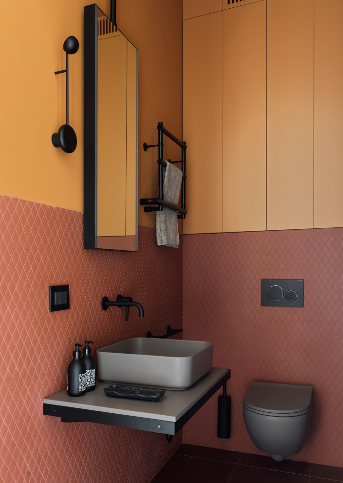 Exemple d'un WC suspendu tendance de taille moyenne avec un mur orange, une vasque, un sol marron, meuble-lavabo suspendu et un plan de toilette gris.