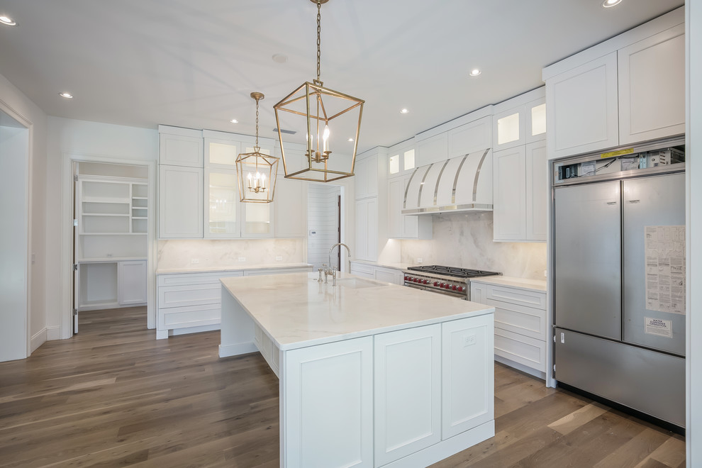 Inspiration for a large transitional l-shaped open plan kitchen in Jacksonville with an undermount sink, shaker cabinets, white cabinets, marble benchtops, white splashback, marble splashback, stainless steel appliances, medium hardwood floors, with island, brown floor and white benchtop.