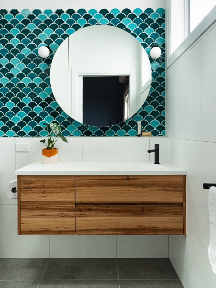 Mid-sized midcentury master bathroom in Melbourne with flat-panel cabinets, medium wood cabinets, an open shower, a wall-mount toilet, blue tile, porcelain tile, white walls, porcelain floors, an integrated sink, solid surface benchtops, grey floor, an open shower, white benchtops, a single vanity and a floating vanity.