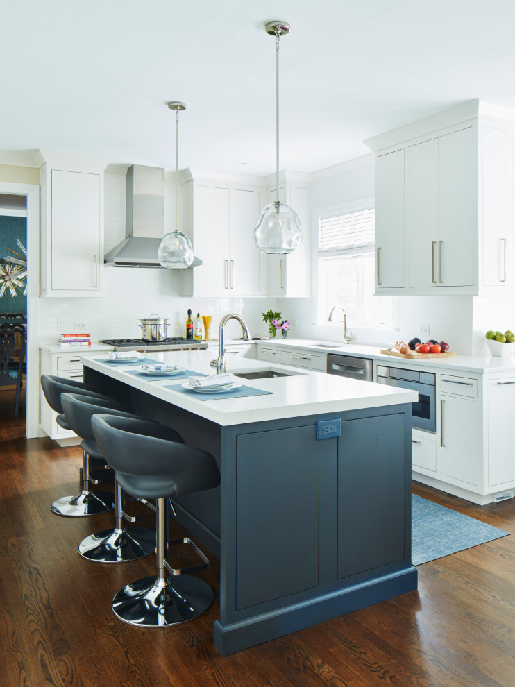 Inspiration for a mid-sized transitional l-shaped eat-in kitchen in New York with an undermount sink, flat-panel cabinets, white cabinets, white splashback, subway tile splashback, stainless steel appliances, medium hardwood floors, with island, brown floor and white benchtop.