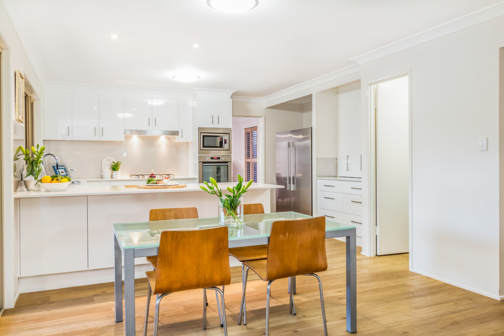 This is an example of a contemporary kitchen/dining combo in Brisbane with white walls and light hardwood floors.