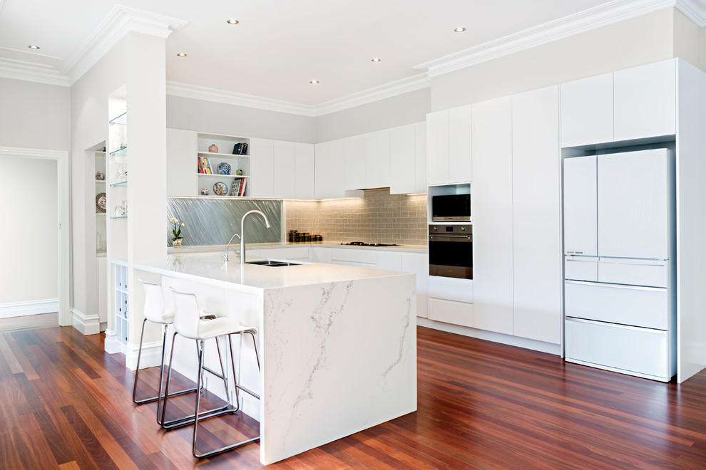 Design ideas for a contemporary u-shaped kitchen in Melbourne with a double-bowl sink, flat-panel cabinets, white cabinets, brown splashback, subway tile splashback, white appliances, medium hardwood floors, a peninsula and red floor.