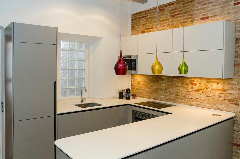 Small modern u-shaped open plan kitchen in Barcelona with an undermount sink, flat-panel cabinets, grey cabinets, solid surface benchtops, brown splashback, brick splashback, stainless steel appliances, ceramic floors, no island and beige benchtop.