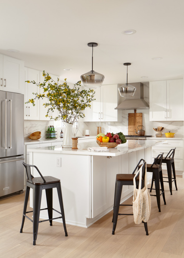 Inspiration for a mid-sized transitional l-shaped eat-in kitchen in San Francisco with an undermount sink, shaker cabinets, white cabinets, quartz benchtops, white splashback, porcelain splashback, stainless steel appliances, light hardwood floors, with island, brown floor and white benchtop.