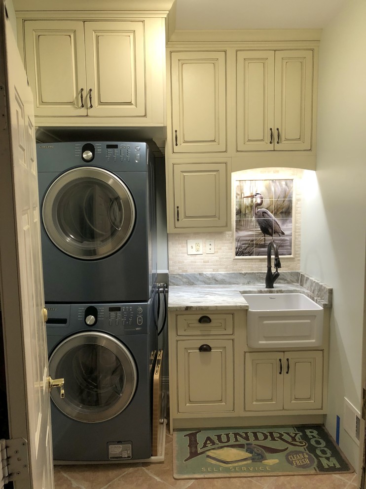 Inspiration for a small beach style single-wall dedicated laundry room in Baltimore with a farmhouse sink, beaded inset cabinets, distressed cabinets, granite benchtops, green walls, ceramic floors, a stacked washer and dryer, brown floor and brown benchtop.