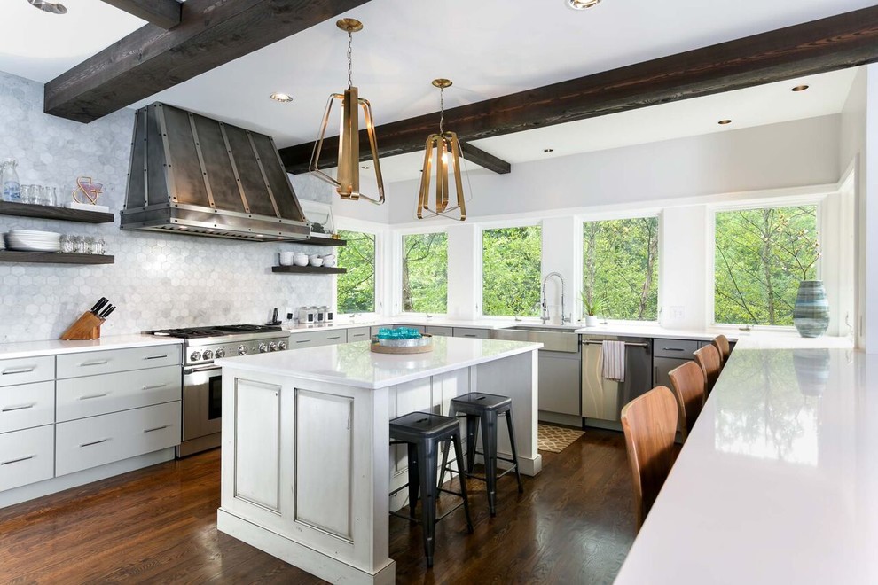 Design ideas for a large transitional u-shaped kitchen in Nashville with flat-panel cabinets, solid surface benchtops, stainless steel appliances, medium hardwood floors, with island, a farmhouse sink, grey cabinets and grey splashback.