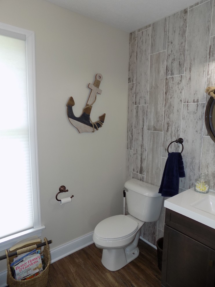 Inspiration for a small beach style 3/4 bathroom in Columbus with recessed-panel cabinets, dark wood cabinets, a drop-in tub, a two-piece toilet, beige tile, ceramic tile, beige walls, medium hardwood floors, an integrated sink, solid surface benchtops and brown floor.