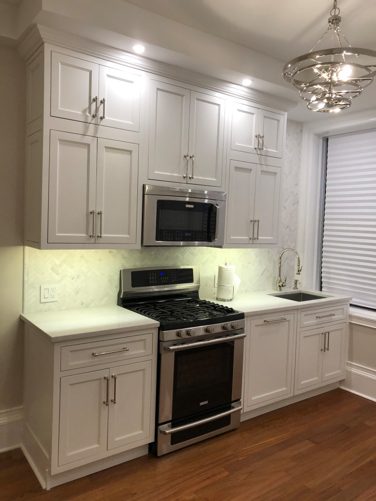 Example of a small transitional galley dark wood floor and brown floor eat-in kitchen design in New York with an undermount sink, recessed-panel cabinets, white cabinets, quartz countertops, multicolored backsplash, marble backsplash, paneled appliances, no island and white countertops