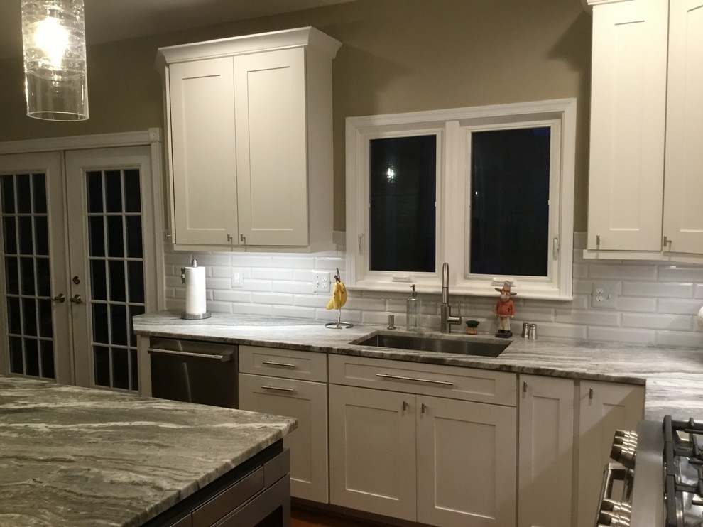 Mid-sized transitional u-shaped medium tone wood floor and brown floor open concept kitchen photo in DC Metro with an undermount sink, white cabinets, granite countertops, white backsplash, subway tile backsplash, stainless steel appliances, an island, gray countertops and shaker cabinets