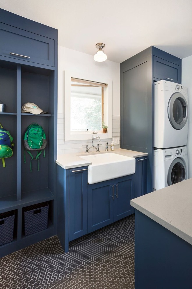 Mid-sized country galley utility room in Austin with a farmhouse sink, shaker cabinets, quartz benchtops, white walls, porcelain floors, a stacked washer and dryer, black floor and blue cabinets.