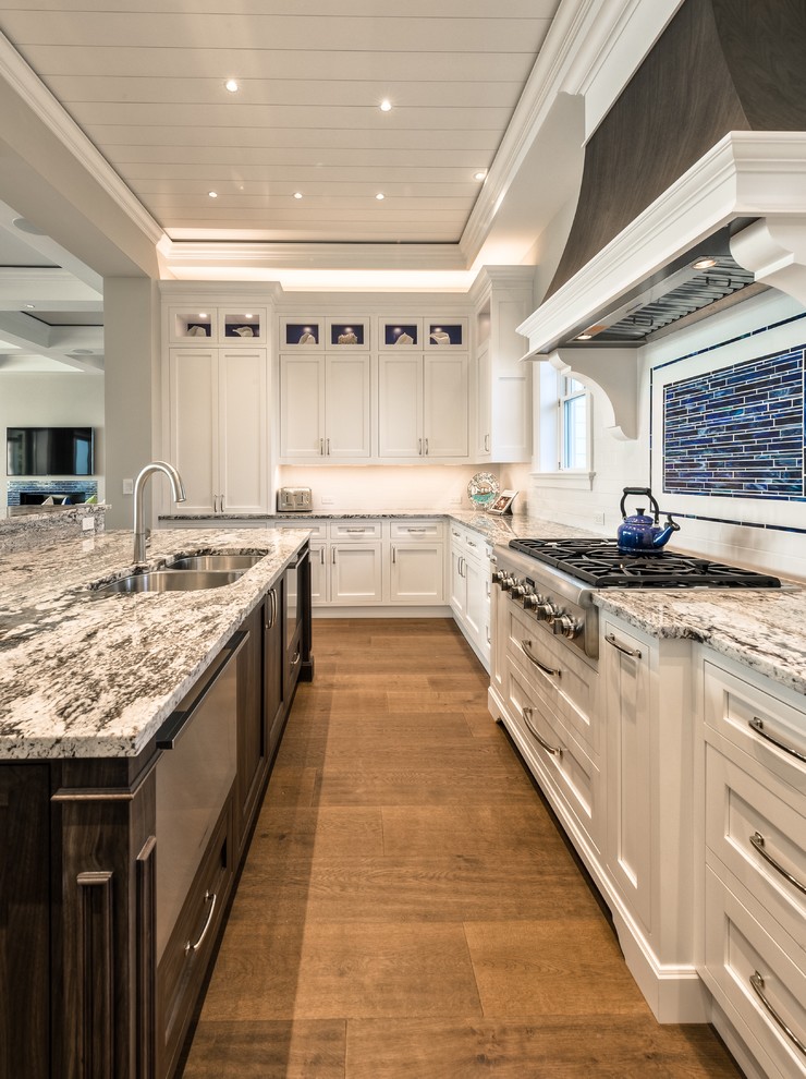 Inspiration for a large beach style u-shaped eat-in kitchen in Miami with an undermount sink, shaker cabinets, white cabinets, quartzite benchtops, white splashback, subway tile splashback, stainless steel appliances, medium hardwood floors and with island.
