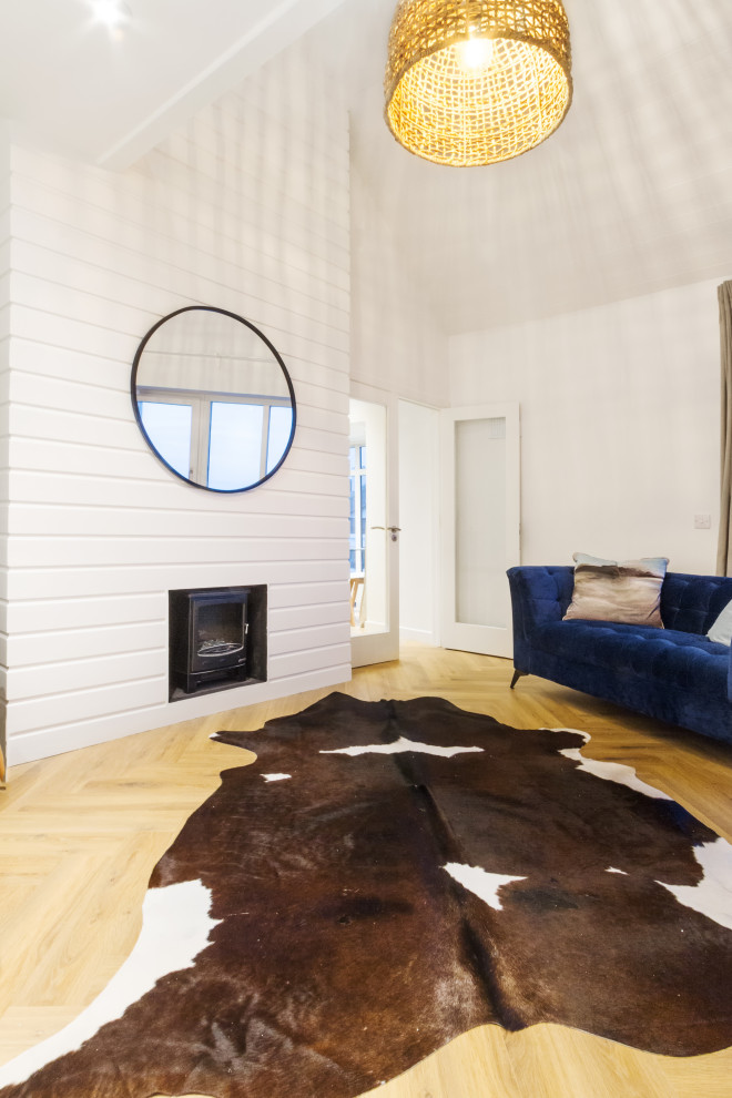 Cette photo montre un salon mansardé ou avec mezzanine bord de mer de taille moyenne avec un mur blanc, sol en stratifié, un manteau de cheminée en lambris de bois, un sol beige, un plafond en bois et du lambris de bois.