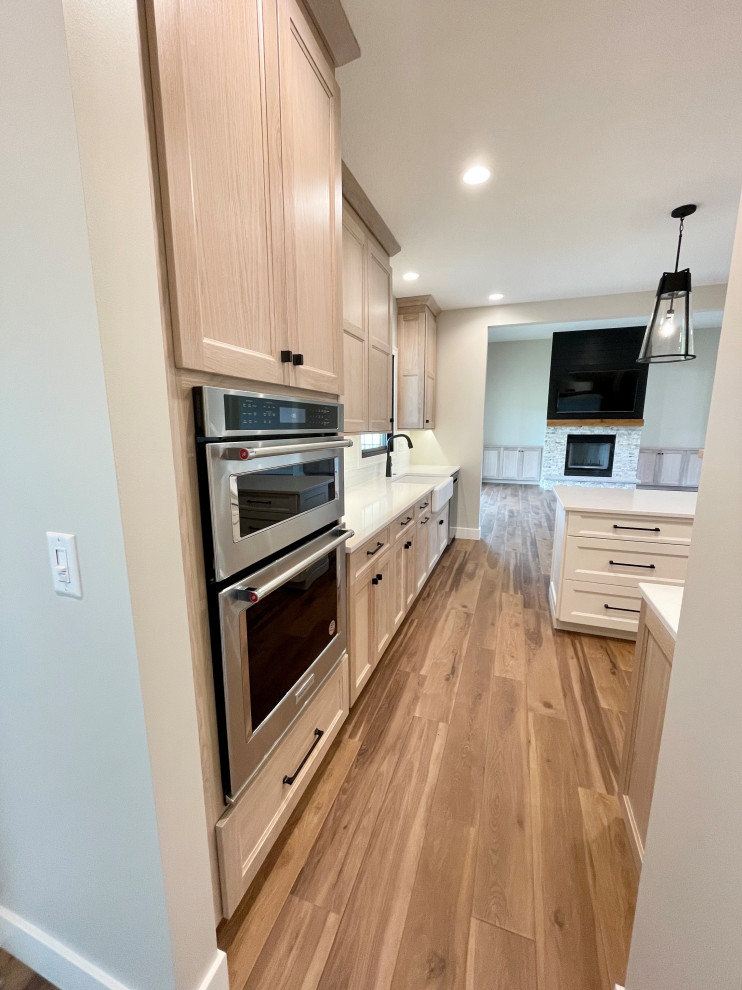 Large danish u-shaped vinyl floor and multicolored floor open concept kitchen photo in Other with a farmhouse sink, flat-panel cabinets, light wood cabinets, quartz countertops, white backsplash, porcelain backsplash, stainless steel appliances, an island and white countertops