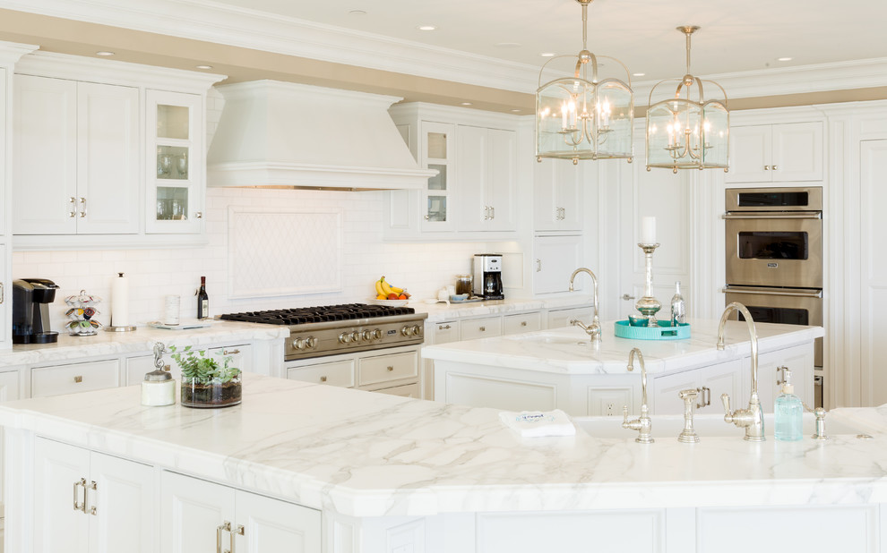 This is an example of a beach style kitchen in Orange County with white cabinets, marble benchtops and white splashback.