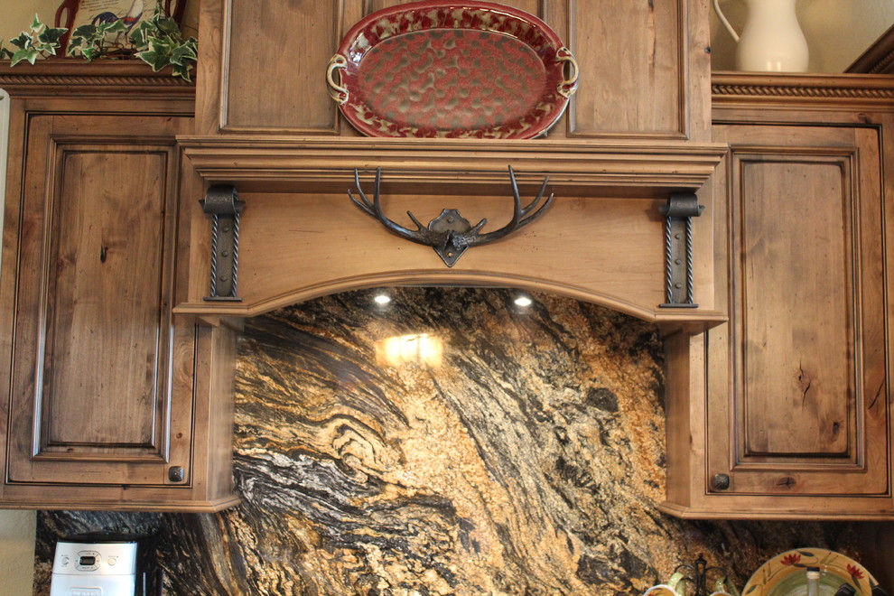Example of a mid-sized mountain style medium tone wood floor enclosed kitchen design with an undermount sink, raised-panel cabinets, medium tone wood cabinets, granite countertops, multicolored backsplash, stone slab backsplash, stainless steel appliances and an island