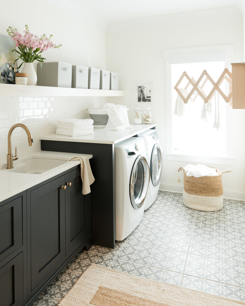 Transitional single-wall dedicated laundry room in Charlotte with an undermount sink, shaker cabinets, black cabinets, white walls, a side-by-side washer and dryer, multi-coloured floor and white benchtop.