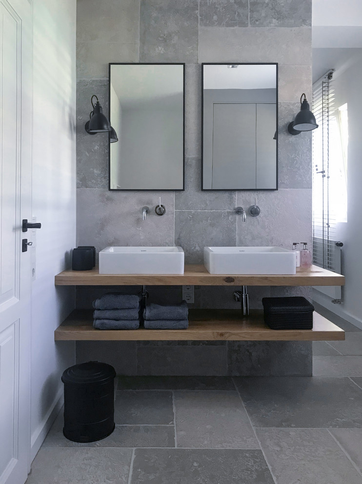 Inspiration for a small contemporary bathroom in Frankfurt with a freestanding tub, a curbless shower, a wall-mount toilet, gray tile, a vessel sink, grey floor, open cabinets, light wood cabinets, white walls and wood benchtops.
