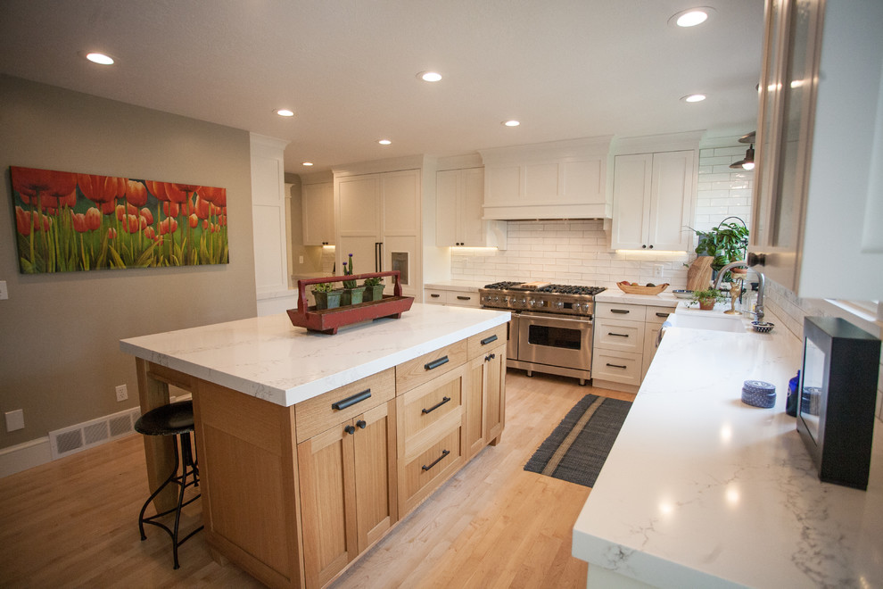 This is an example of a mid-sized transitional l-shaped open plan kitchen in Salt Lake City with a farmhouse sink, shaker cabinets, medium wood cabinets, marble benchtops, white splashback, ceramic splashback, panelled appliances, light hardwood floors and with island.