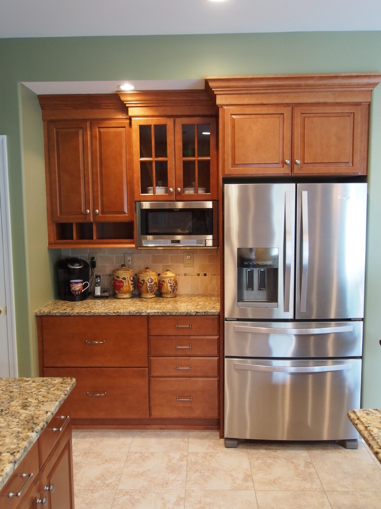 Example of a large transitional l-shaped ceramic tile eat-in kitchen design in New York with an undermount sink, raised-panel cabinets, medium tone wood cabinets, granite countertops, beige backsplash, stone tile backsplash, stainless steel appliances and an island