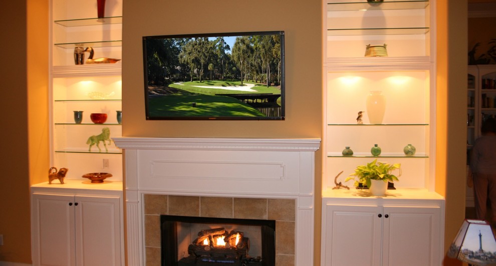 Photo of a mid-sized beach style formal enclosed living room in Atlanta with beige walls, medium hardwood floors, a standard fireplace, a tile fireplace surround, a wall-mounted tv and brown floor.