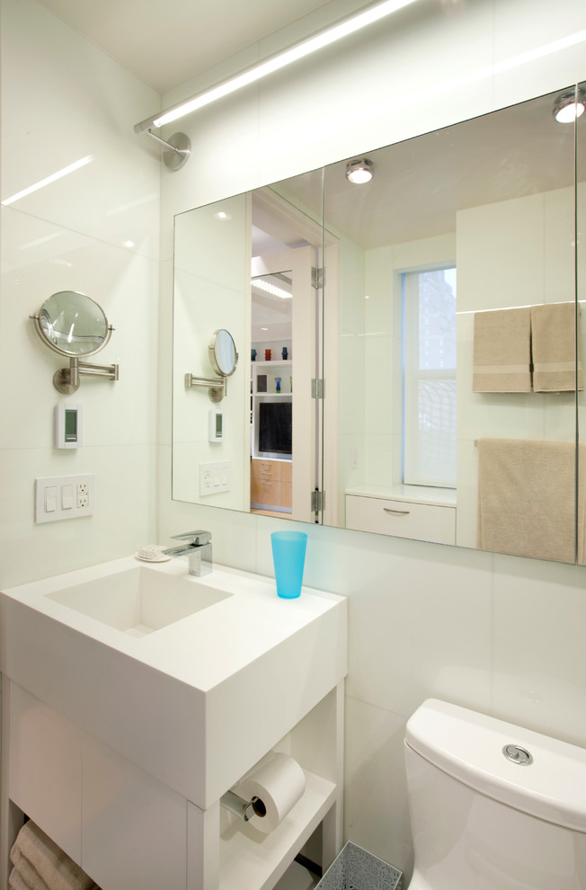 This is an example of a small modern 3/4 bathroom in New York with flat-panel cabinets, white cabinets, an alcove shower, a one-piece toilet, white tile, porcelain tile, white walls, concrete floors, a console sink, grey floor and a hinged shower door.